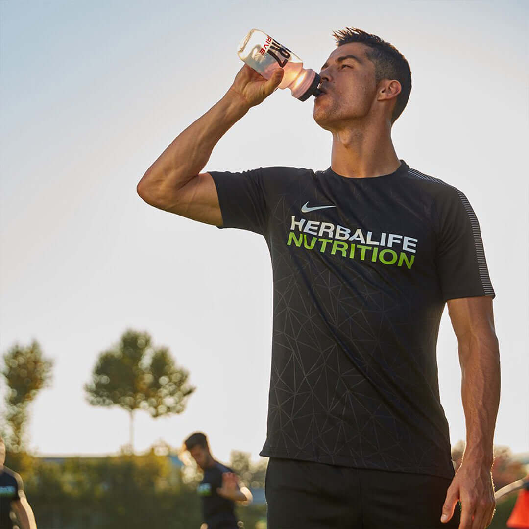 Atleta con maglietta Herbalife Nutrition che beve una bevanda sportiva all'aperto durante un allenamento.