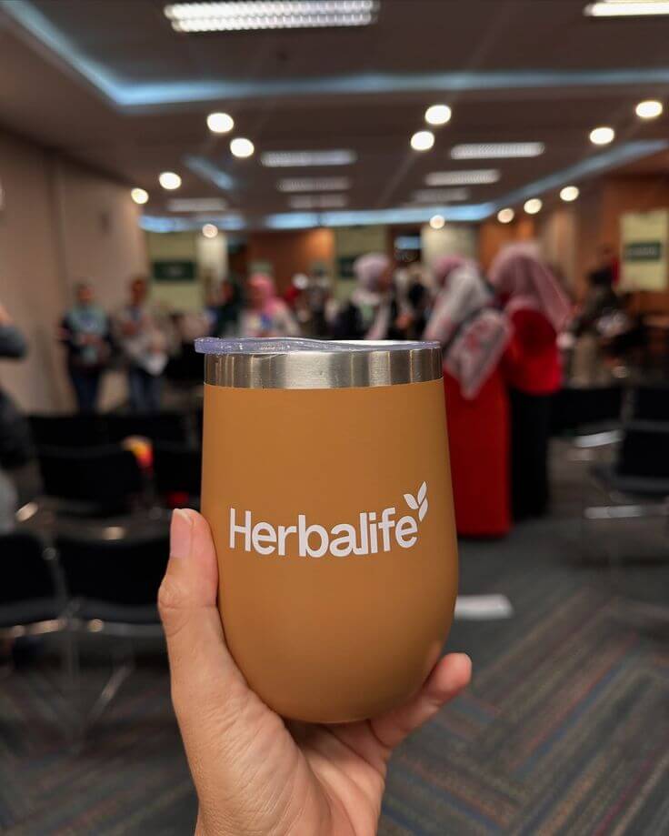 A hand holding a Herbalife tumbler at a crowded event, showcasing wellness community engagement.