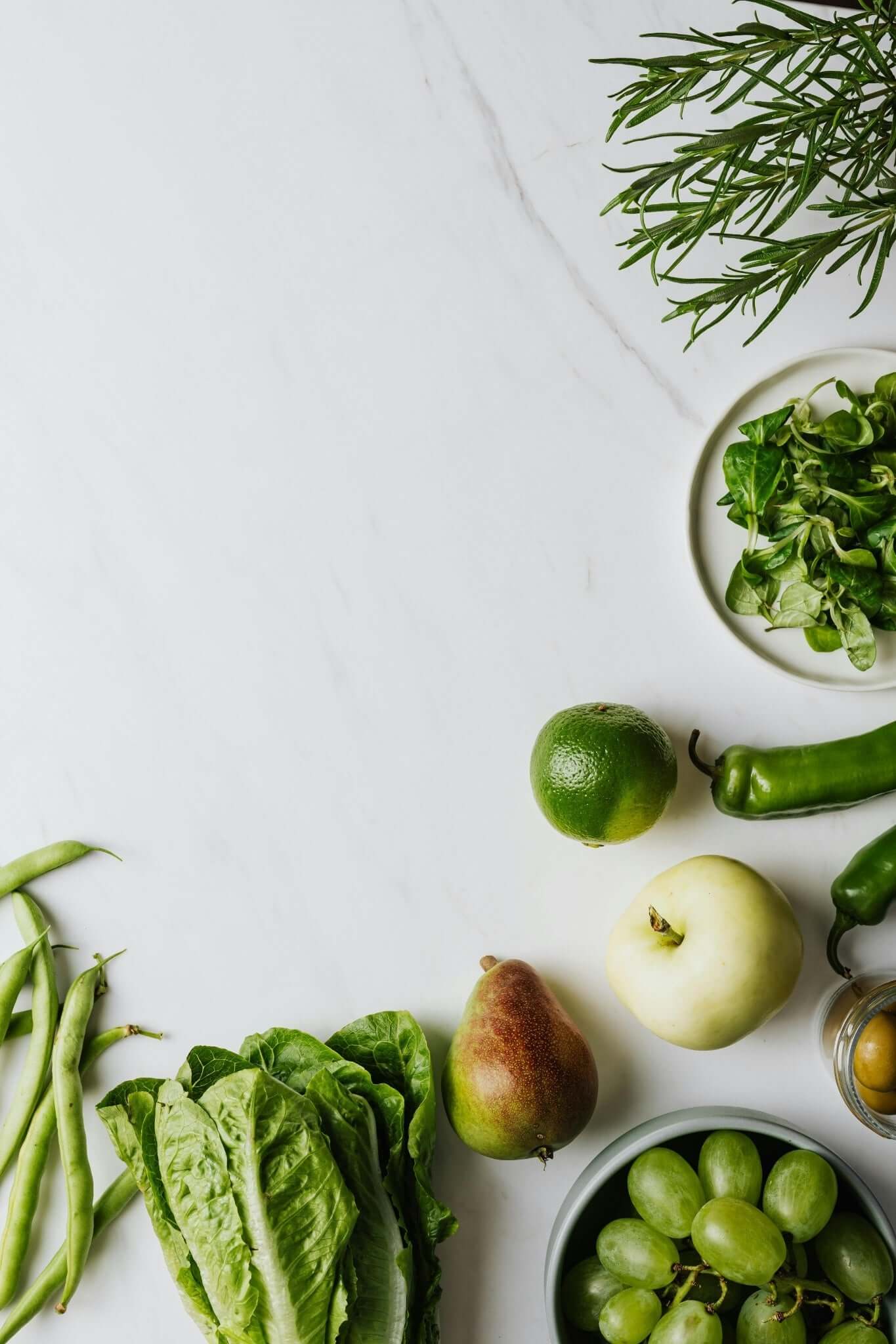 Verdure e frutta fresca disposte su una superficie di marmo, tra cui lime, uva e verdure a foglia.