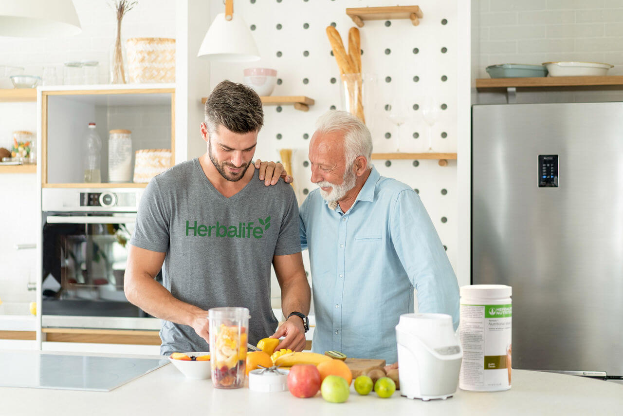 Two men enjoying healthy fruit preparation in a modern kitchen, promoting wellness and active lifestyles.